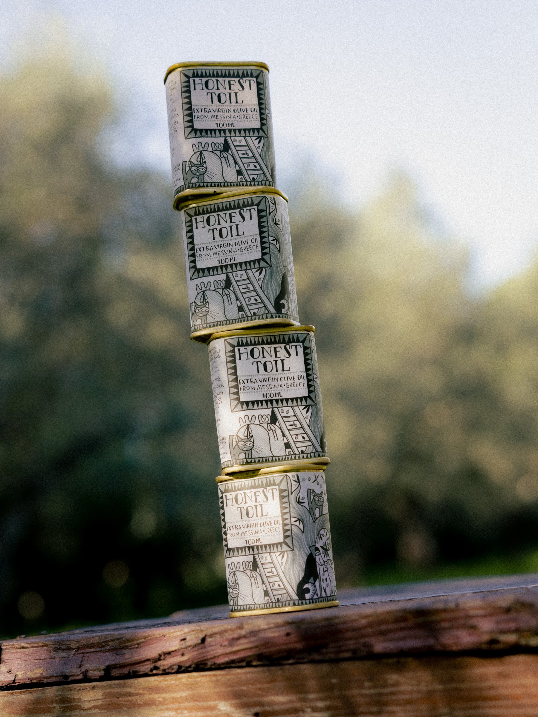 Four Honest Toil 100ml tins stacked on a wooden beam outdoors.